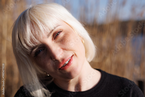 A close-up, detailed portrait of a beautiful young woman, tilting her head back from the bright rays of the sun and smiling sweetly.