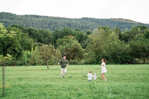 Happy young family with little son playing with kite in field. Healthy childhood.