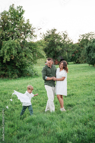 Happy young family with little son playing with kite in field. Healthy childhood.