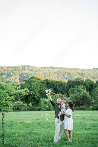 Happy young family with little son playing with kite in field. Healthy childhood.