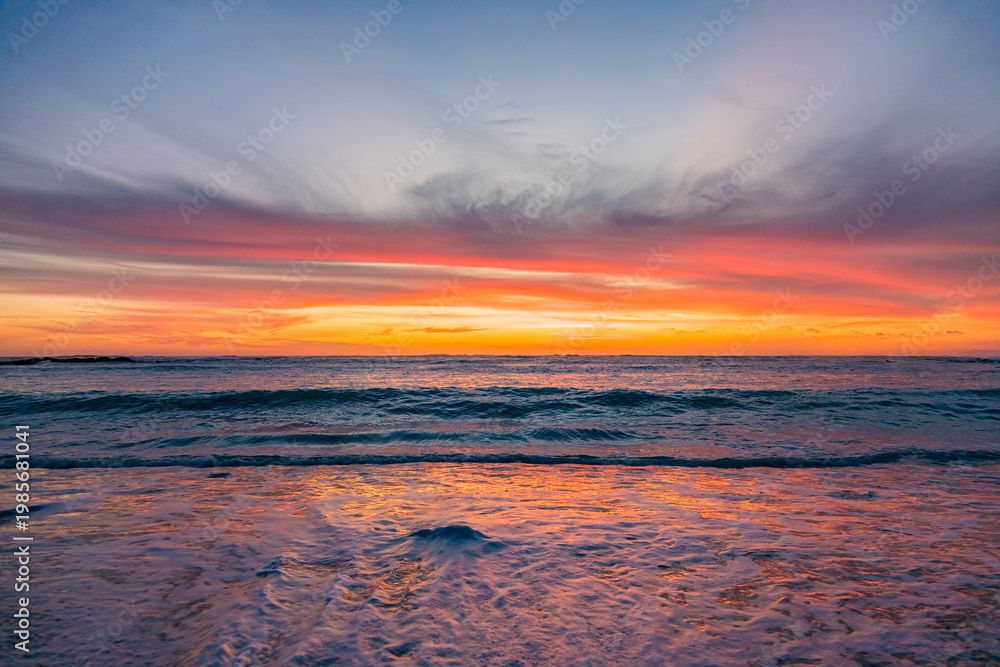 Obraz premium Dramatic Golden sunset over tranquil beach, waves lashing the pebble coastline