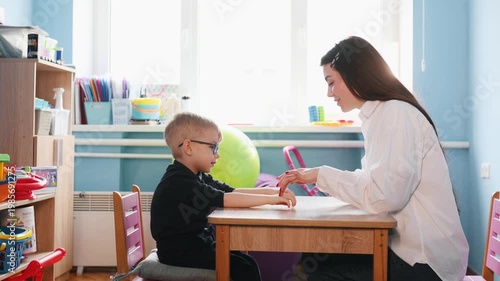 female therapist and boy practicing hand gestures in therapy session, concept of child development and alternative communication