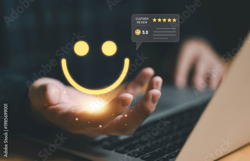 Hand holding glowing smiley face with 5-star customer review rating over laptop, representing customer satisfaction, positive feedback, and digital experience in modern business and online services.