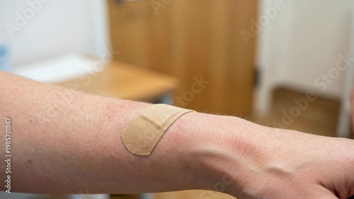 Hand applying adhesive bandage on arm wound, closeup healthcare scene showing first aid, injury care, hygiene, safety, treatment, and home medical routine.