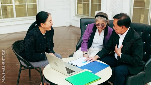 Advisor meeting with senior clients at a table, reviewing documents and a laptop during a financial planning consultation.