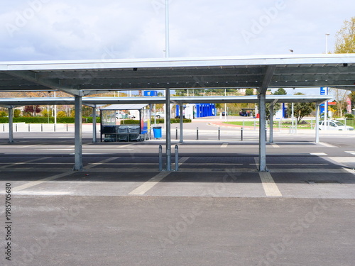 Parking area shows several covered spots without any cars present. Shopping center can be seen in the background. The weather is clear with some clouds in the sky