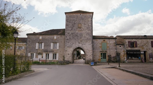 Historic stone gatehouse tower marking the entrance to Monpazier in Dordogne. Slow motion tracking shot towards the archway.
