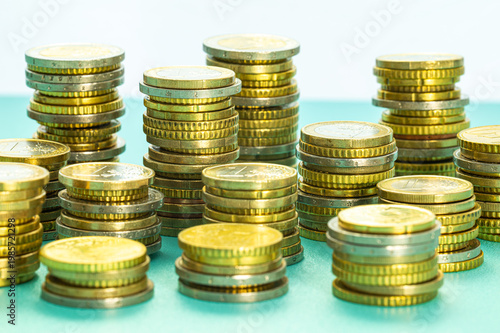 Stacks of coins next to each other, on light blue surface. Amount of money and wealth.