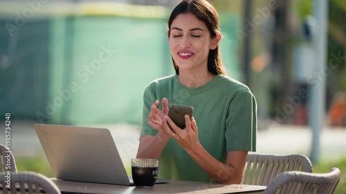 Video of happy businesswoman working with laptop while talking with smartphone having a drink on a terrace in the city