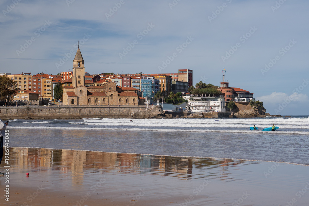Obraz premium Panoramic view of San Lorenzo beach with San Pedro church reflection on wet sand. Gijon, Asturias, Northern Spain.