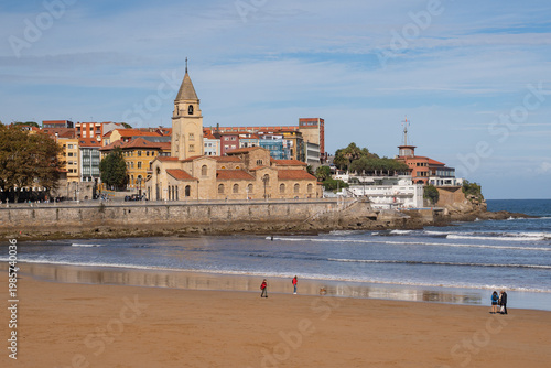 San Pedro Church and San Lorenzo beach with surfers at sunset in Gijon, Asturias, Spain.