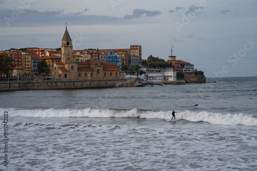 San Pedro Church and San Lorenzo beach with surfers at sunset in Gijon, Asturias, Spain.