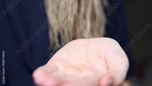 Female applying hair product from a spray bottle into her palm, preparing to style her wet hair while wearing a dark shirt in a softly lit indoor setting