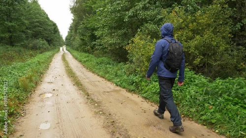 Hiker walking along muddy forest road after rainfall in lush green woodland