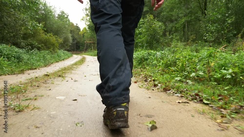 Hiker walking on wet forest path with muddy ground and green vegetation