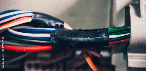 Multicolored electrical wires bundled and secured with black tape, inserted into metal connector, close-up view.