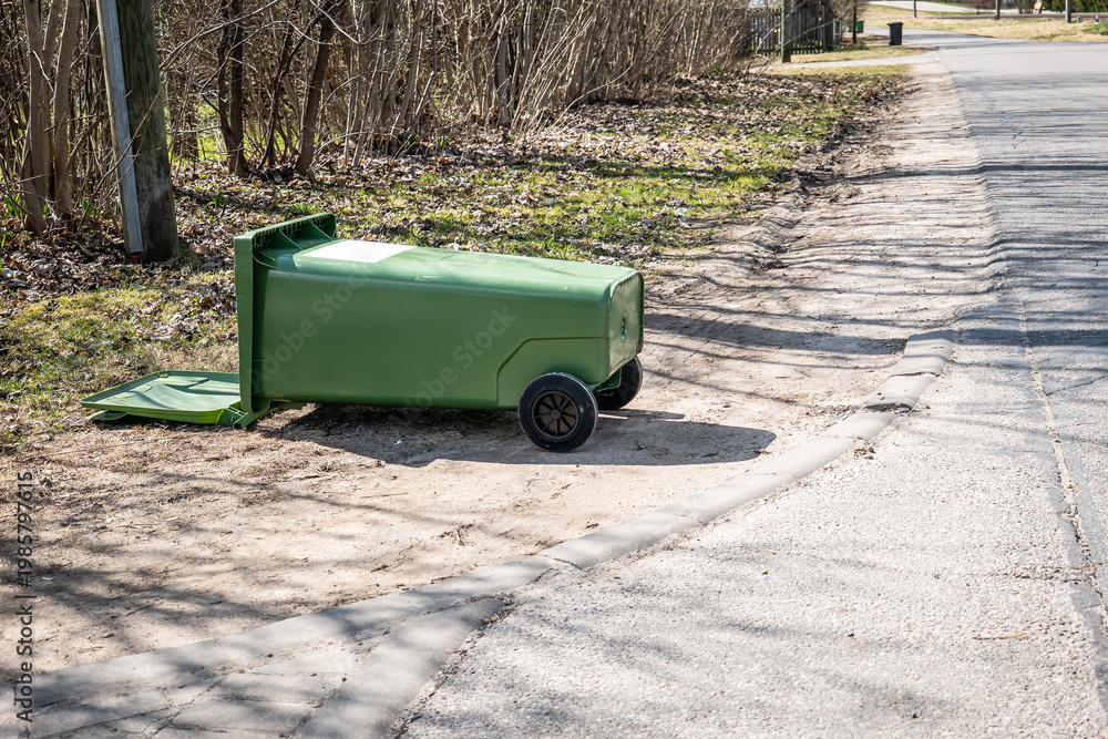 Fototapeta premium Green Garbage Bin Lying on Side Near Roadside with Open Lid Outdoors