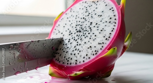 Close-up of a vibrant dragon fruit being sliced in half with a sharp knife.