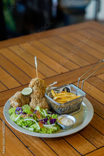 Crispy fried chicken served with french fries, fresh salad, and dipping sauce on wooden table. Vertical composition with copy space, ideal for restaurant ads and menu design.