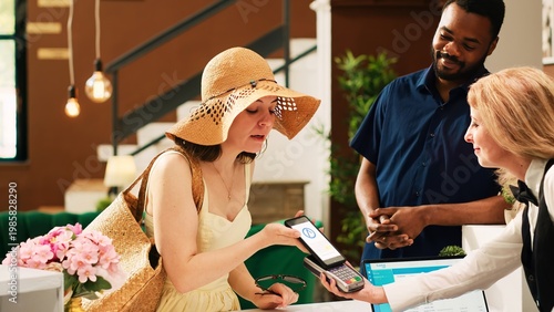 Fotografie Guests doing mobile nfc payment on pos terminal in lobby, using smartphone and paying for room at tropical seaside hotel