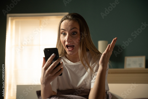 Fotografía Woman in bedroom reacting with disbelief and astonishment while reading shocking