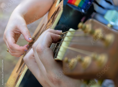 Quadro su tela Close up of woman playing a guitar from the side with only hands and arms visibl