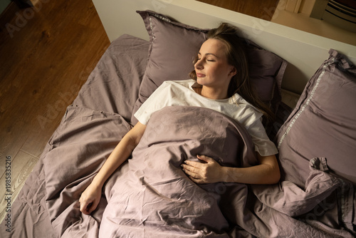 Young woman resting soundly in a cozy bed, finding comfort and tranquility under soft lilac bedding, creating a serene and quiet atmosphere for a rejuvenating sleep