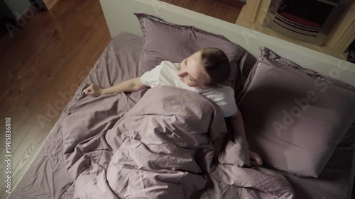 Happy young woman waking up in a comfortable cozy bed, stretching her arms and smiling as she greets the new day in her sunlit bedroom. High angle view capturing a moment of blissful awakening