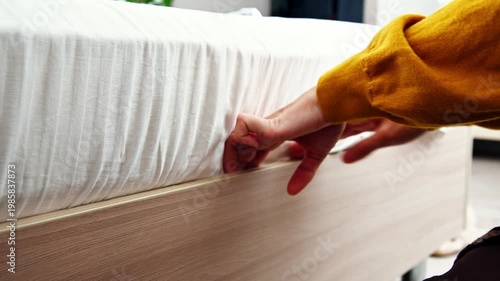 Person adjusting fitted sheet on bed frame in bright, modern bedroom setting