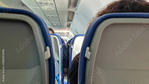 Interior of airplane cabin with passengers seated during flight, view between seats in economy class. Travel concept with air transportation, journey, and modern aviation lifestyle.