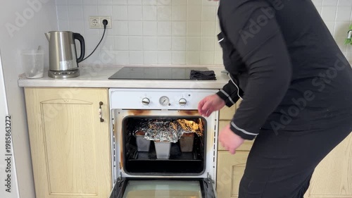 A woman with dark curly hair takes freshly baked loaves of bread out of a hot oven. She uses an oven mitt for protection and places the hot bread on the kitchen counter to cool. Domestic life scene