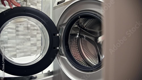 Opening washing machine door to load laundry in modern bathroom setting