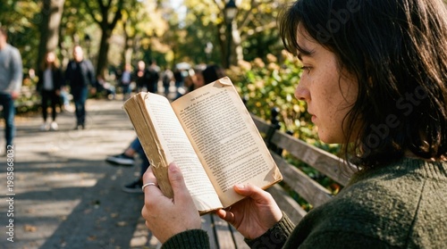 Young Woman Reading a Physical Novel on a Park Bench in Sunlight