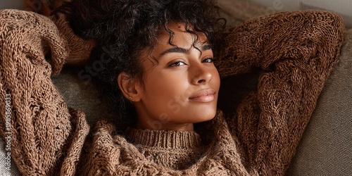 A woman in a brown sweater is relaxing while sitting on a sofa at home