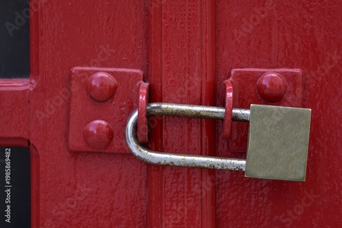 Closeup view of a Carmine red wooden entrance door with a stainless steel long shackle rustproff padlock.