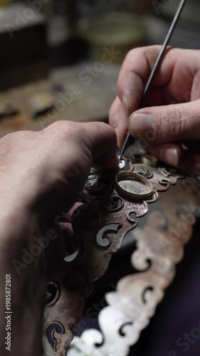 Jeweler crafting ornate silver crown with fleur-de-lis motif and detailed patterns in workshop. Traditional jewelry making process in workshop environment
