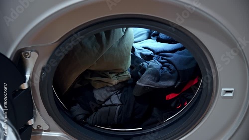 Hand placing dirty laundry into washing machine, close-up view of clothes