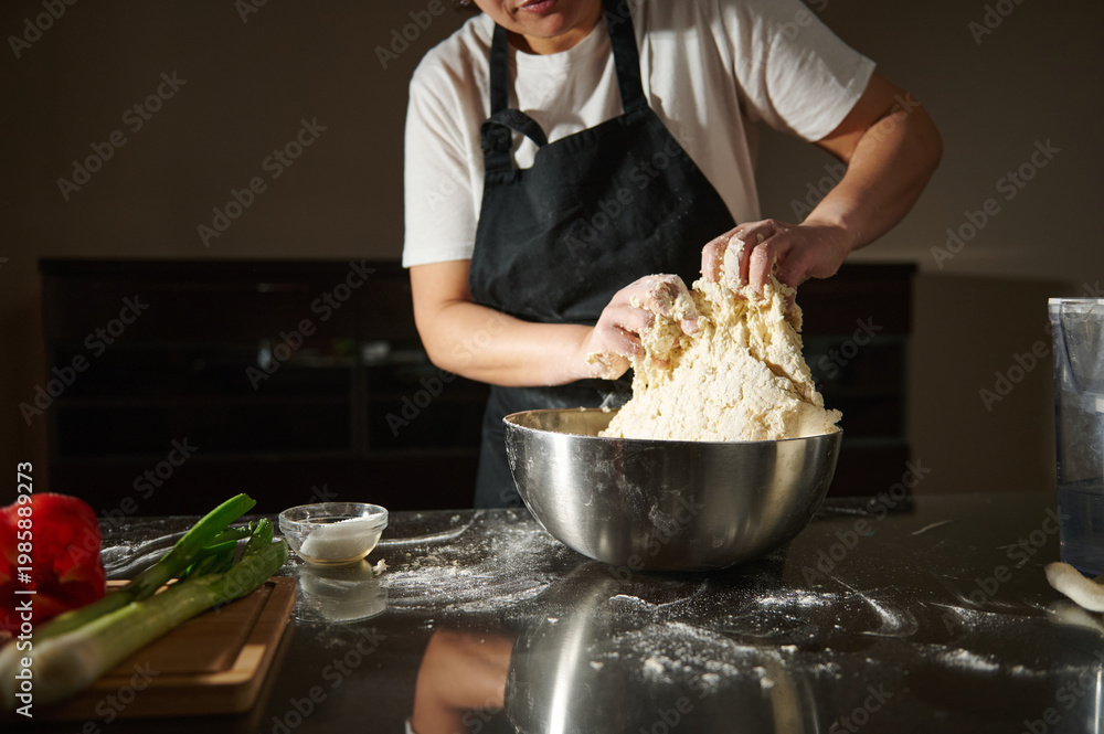 © Taras Grebinets - Home Baker Kneading Dough in Kitchen With Apron and Stainless Steel Mixing Bowl