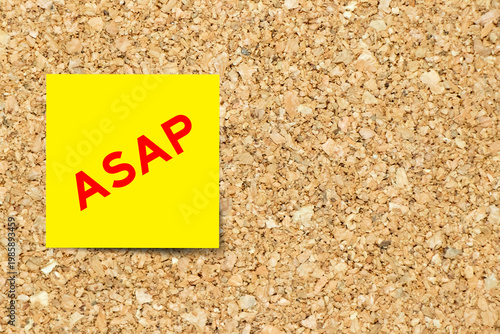 Yellow note paper with word ASAP (Abbreviation of as soon as possible) on cork board background with copy space