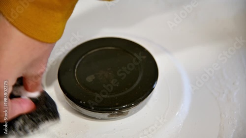 Hand scrubbing black plate on white surface, cleaning process in kitchen