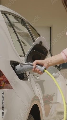 A woman charges a white electric vehicle at a station with a bright yellow cable, promoting renewable energy for eco-friendly transportation.
