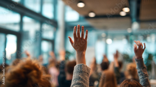A diverse group of people actively participate in a seminar, raising their hands to ask questions or contribute ideas. The modern conference room is filled with natural light and energy