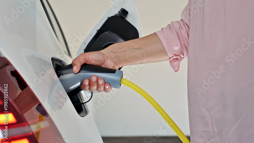 Foto A woman, with her ethnicity not discernible, is seen holding the charging plug of an electric vehicle, preparing to connect it to the charging station
