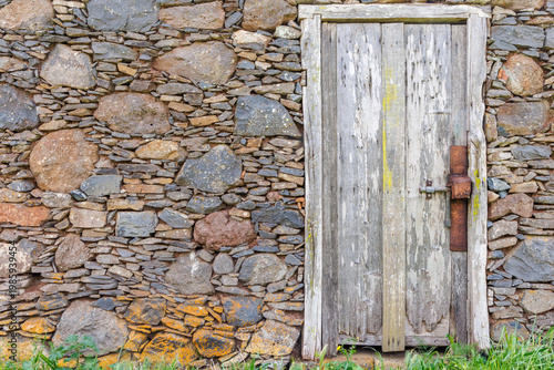 Old weathered wooden door in a traditional rustic stone wall on La Gomera, ancient architecture with rough textures, lichen and rusty metal latch, Canary Islands