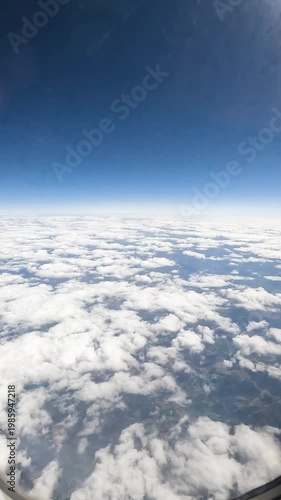 Passenger POV from airplane window showing flight above white cloud layer with deep blue sky and atmospheric gradient.