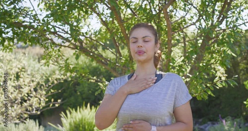 African American woman placing hands on chest, belly breathing in garden wearing sports bra calming