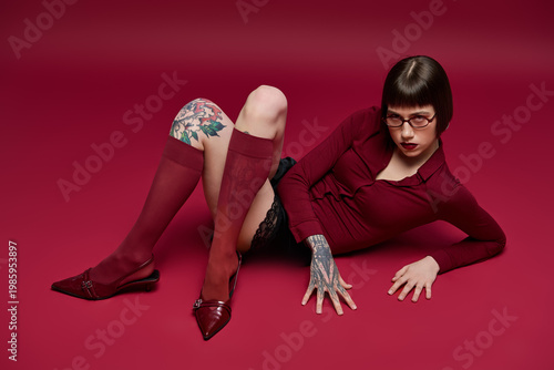 Vászonkép Fashionable young woman lounges in stylish attire against a rich burgundy backdr