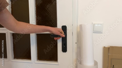 Close-up video of a person's hand grabbing a doorknob and then turning a key in the lock. The scene shows the action of locking or unlocking a white front door in a home or apartment.