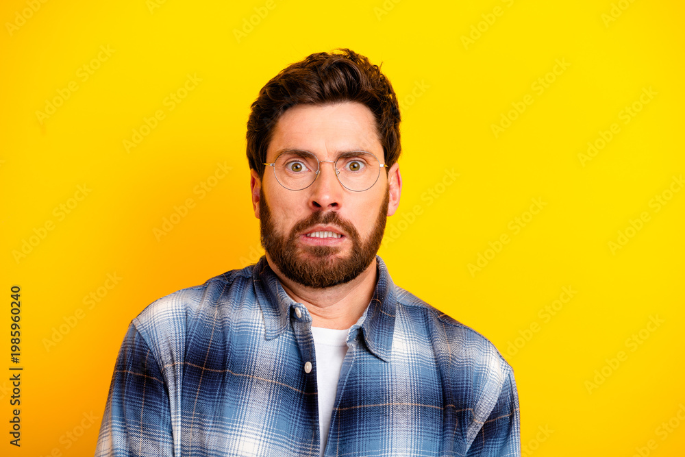 Obraz premium Surprised man with glasses and beard in plaid shirt against bright yellow background showing anxious, shocked facial expression in studio portrait