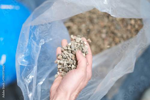 Photos Close up of a builders hand holding gravel aggregate stones from bag for construction and building material selection